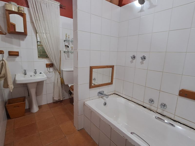A dated bathroom featuring a pedestal basin, built-in bathtub, and ceramic tiling throughout. The space requires cosmetic updates to improve its overall condition.