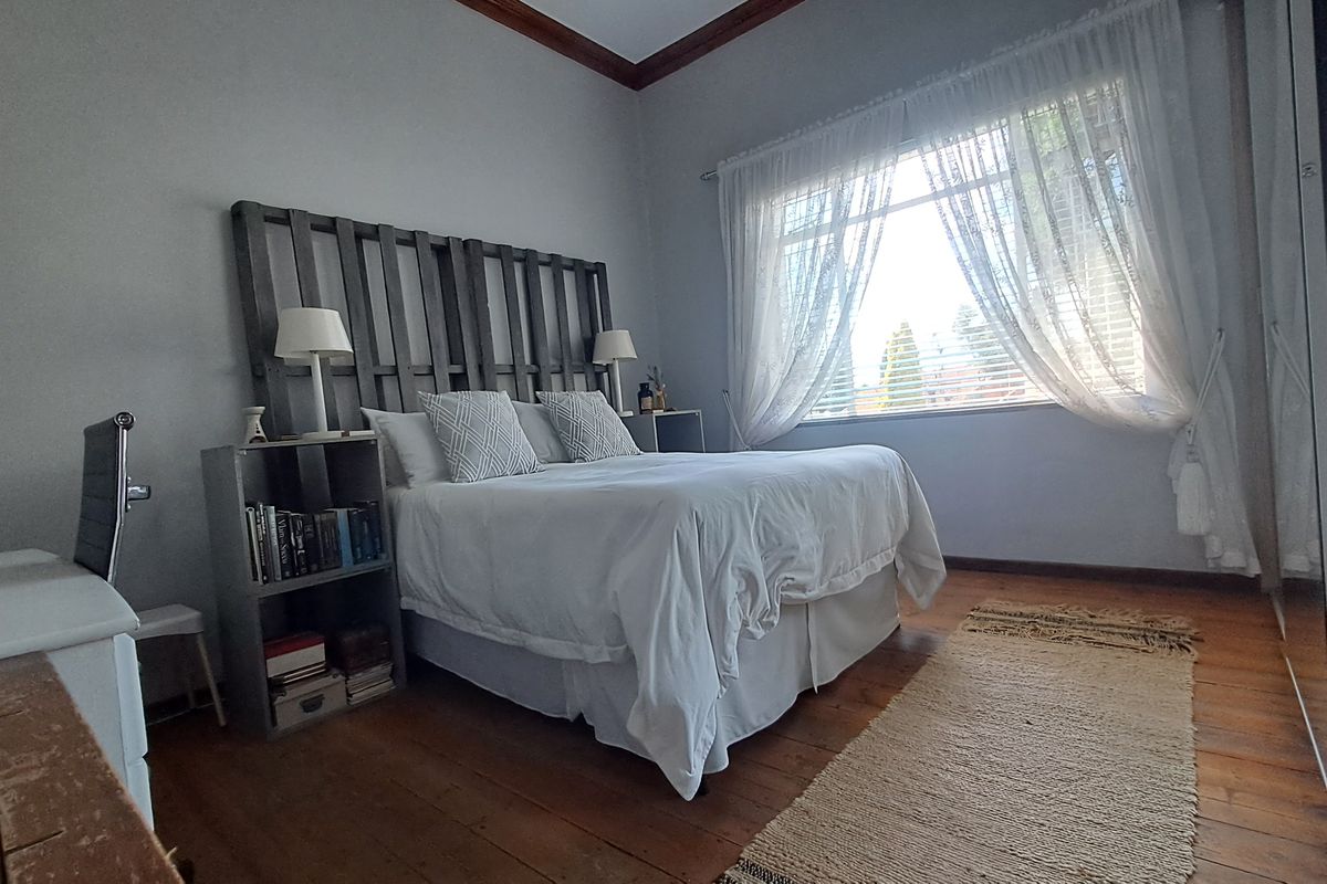 A well-lit bedroom featuring original timber flooring, crown molding, and a large built-in wardrobe with mirrored sliding doors.