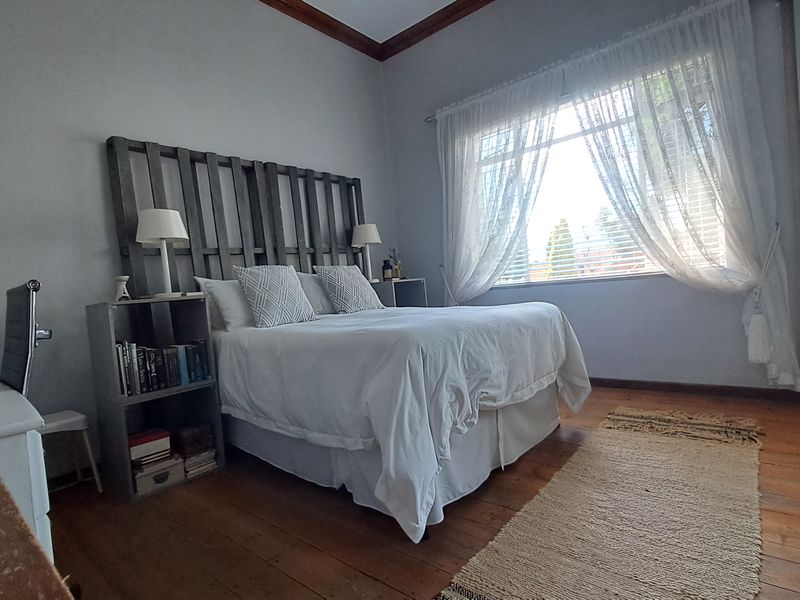 A well-lit bedroom featuring original timber flooring, crown molding, and a large built-in wardrobe with mirrored sliding doors.