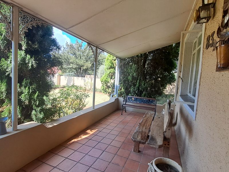 A covered patio area featuring tiled flooring, decorative wrought iron supports, and a low masonry wall overlooking the garden.