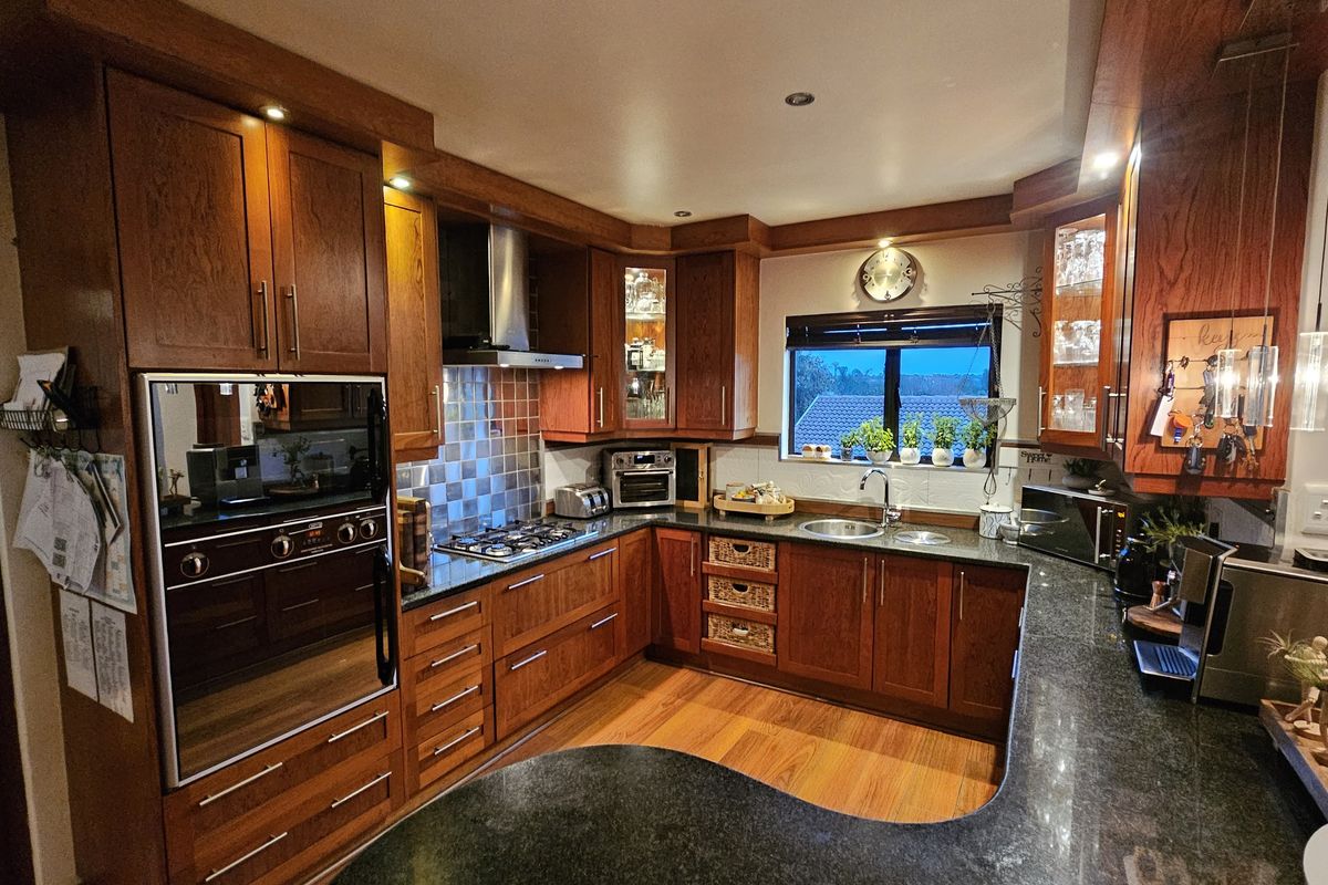A well-appointed kitchen featuring rich wooden cabinetry, granite countertops, a gas hob, and integrated appliances, offering a warm and functional culinary space.