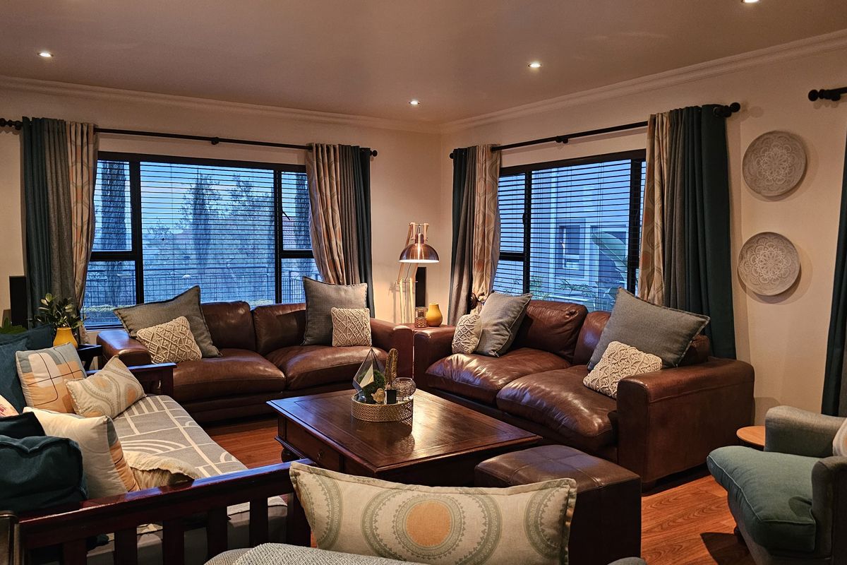 A comfortable and well-maintained living room featuring warm timber flooring, recessed downlighting, and large windows with fitted venetian blinds.