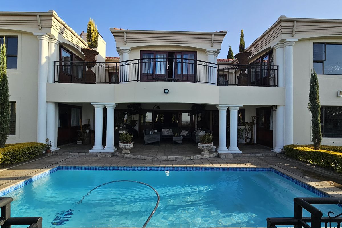 Rear elevation of a double-story residence featuring a swimming pool, covered patio area, and an upper-level balcony with classic architectural columns.