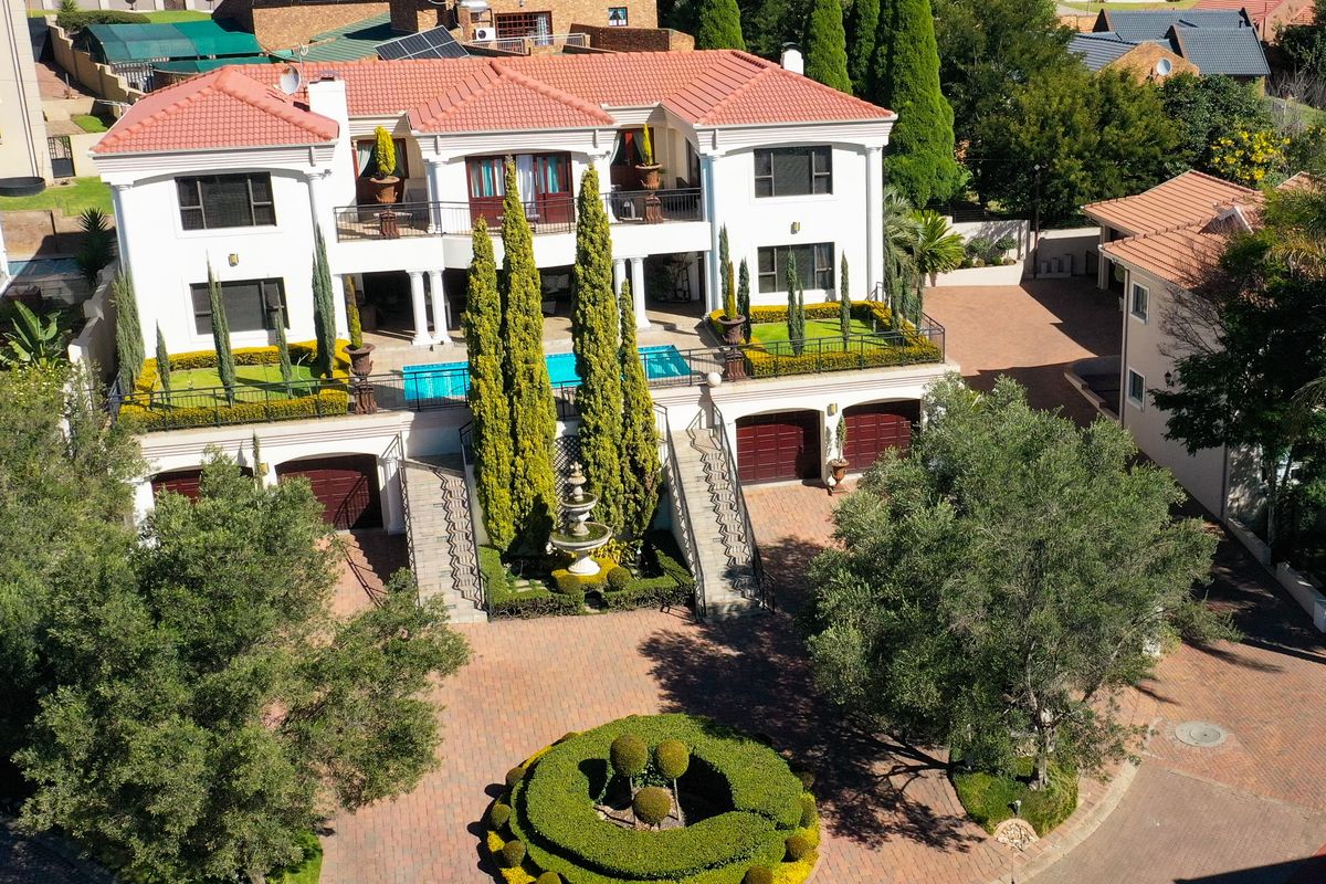 Aerial view of a large multi-story residence featuring a terracotta tiled roof, swimming pool, double garage, and extensive paved driveway with landscaped gardens.