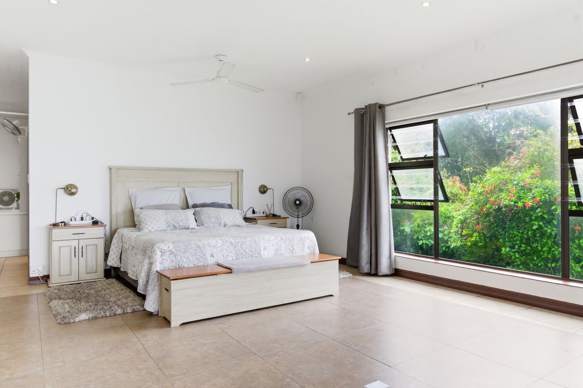 Spacious bedroom featuring large windows with garden views, tiled flooring, recessed ceiling lighting, and a ceiling fan.