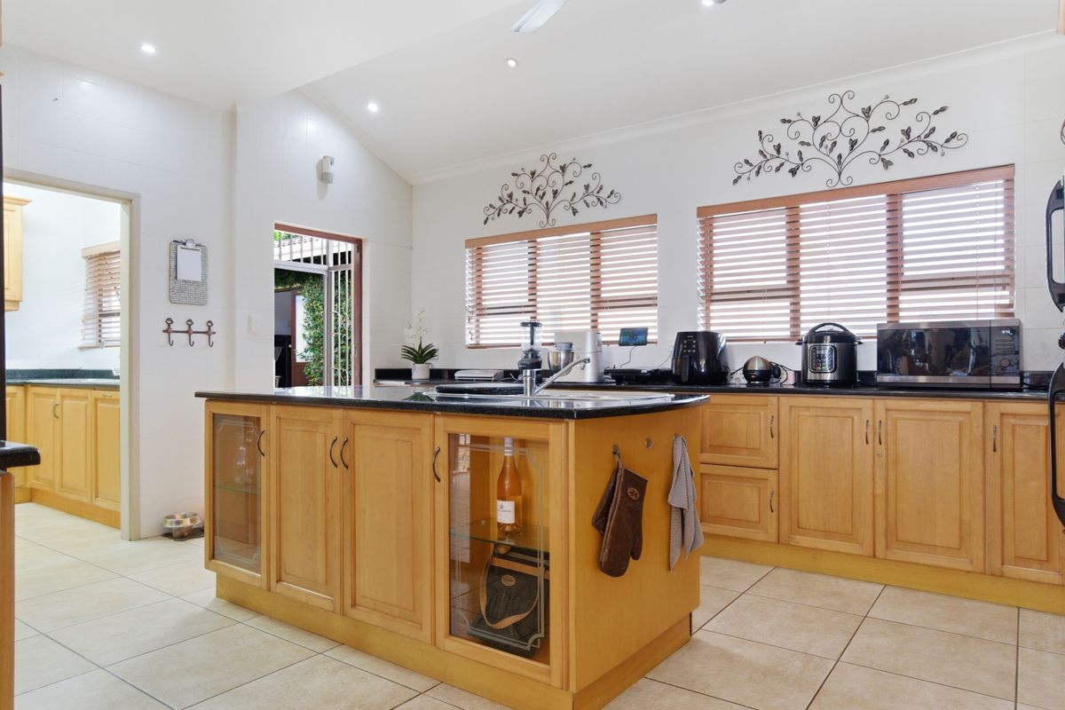 Spacious kitchen featuring light wood cabinetry, a central island with a dark stone countertop, tiled flooring, and recessed ceiling lighting.