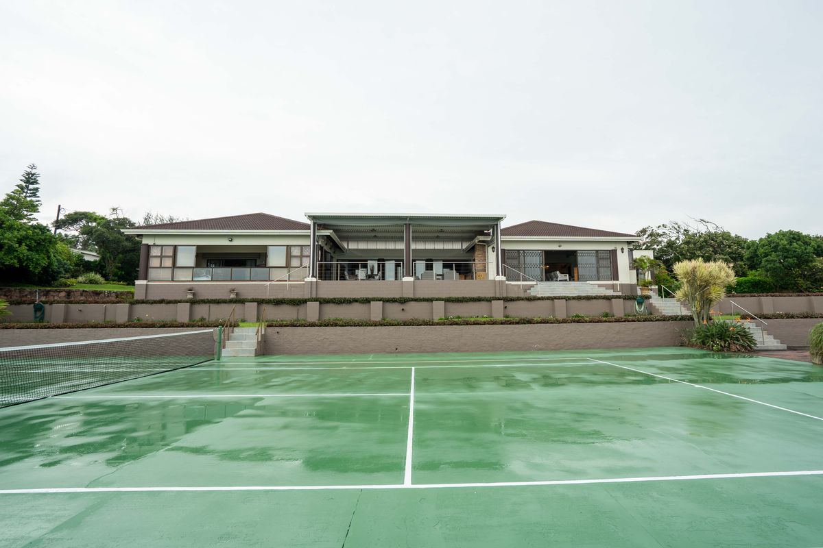Rear view of the property featuring a spacious covered patio and a private tennis court set within the landscaped garden.