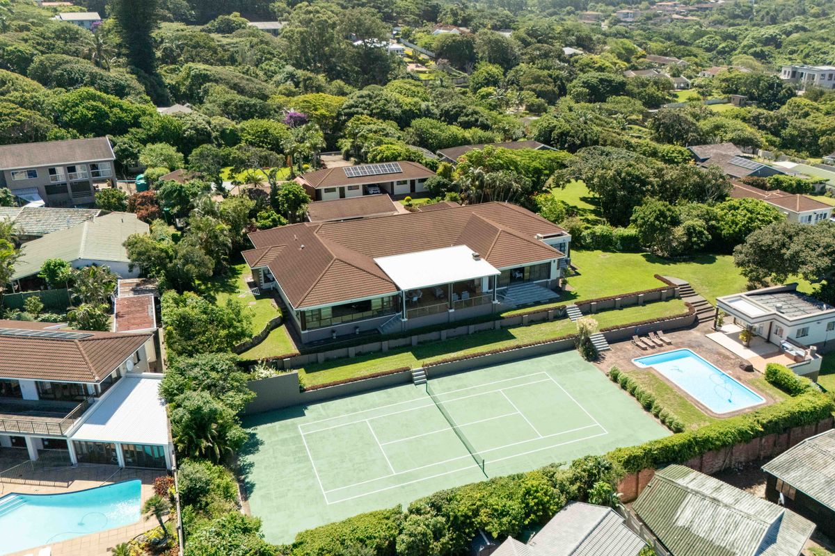 Aerial view of a residential property featuring a large tiled roof house, a private tennis court, a swimming pool, and landscaped garden areas.