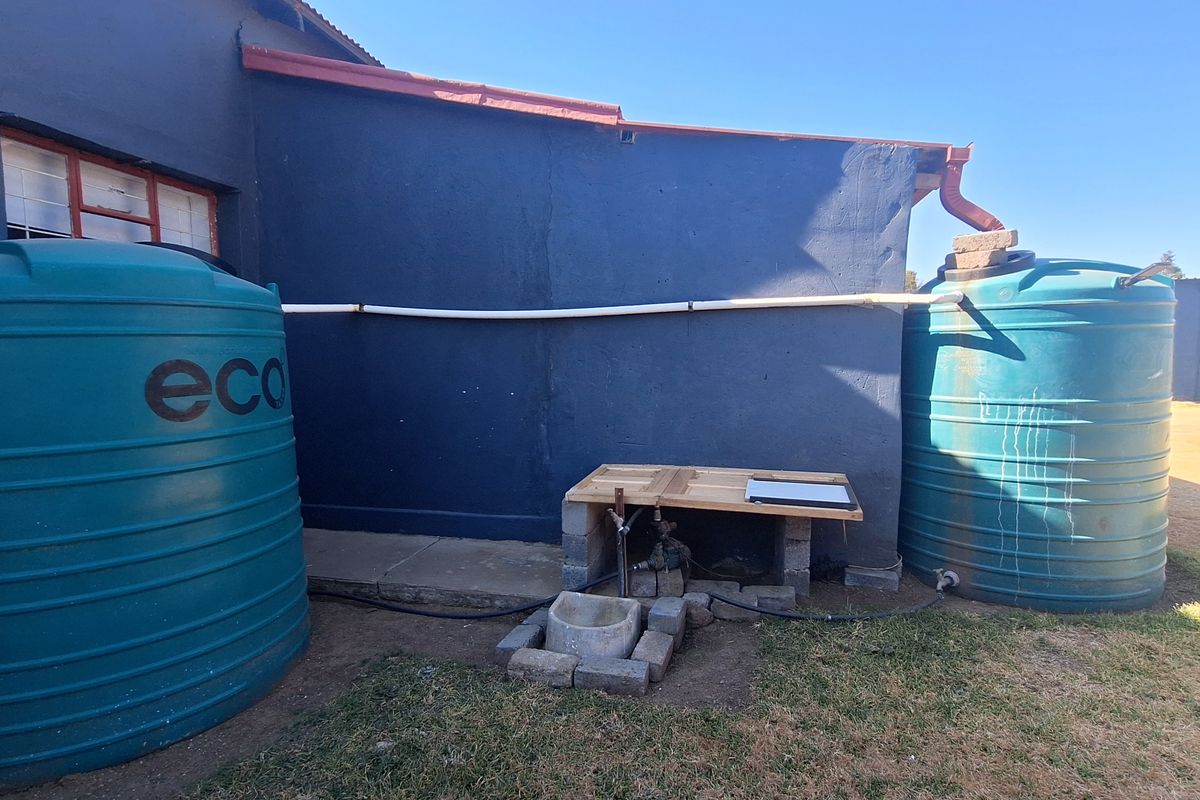 Exterior rear view showing two large water storage tanks connected to the building's gutter system with a small pump installation.