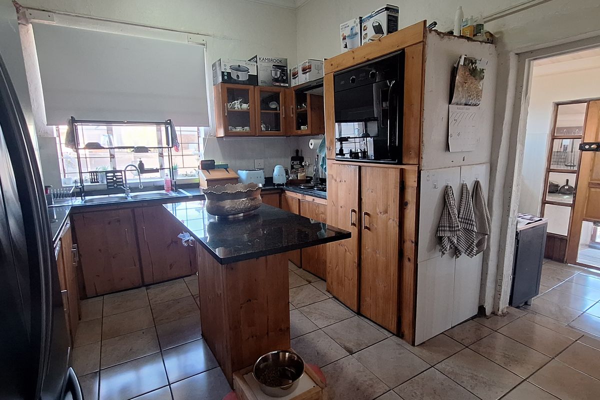 A functional kitchen featuring wooden cabinetry, a central island with a dark stone countertop, tiled flooring, and a built-in oven unit.