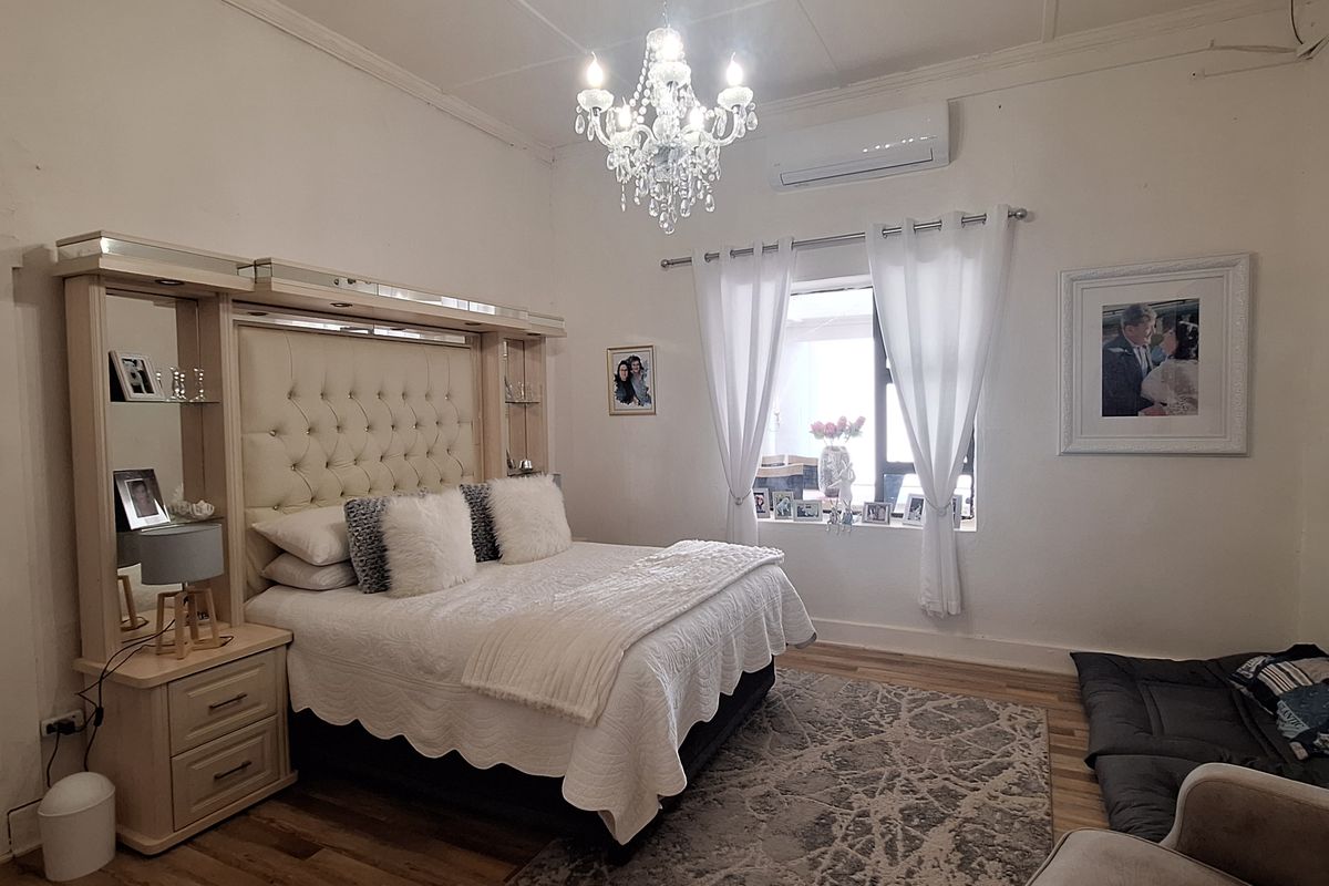 A well-maintained bedroom featuring timber flooring, a split-system air conditioning unit, and a decorative chandelier.