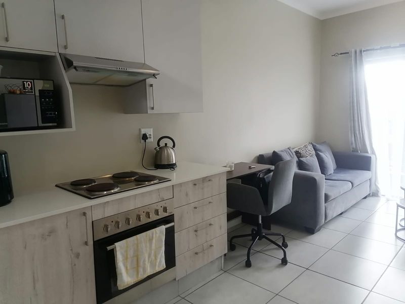 Modern open-plan apartment living area featuring a compact kitchen with built-in appliances and tiled flooring, seamlessly connected to the lounge space.