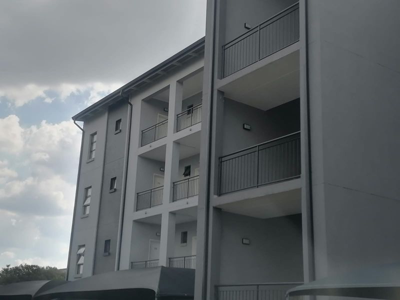 A modern multi-story apartment building facade featuring stacked balconies with metal railings and clean grey exterior finishes.