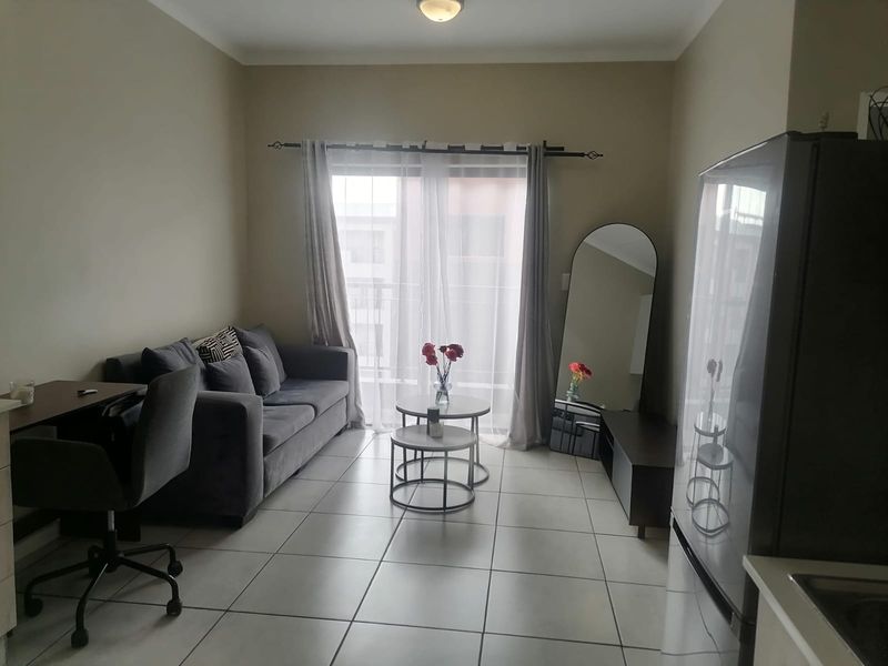 A compact living room featuring neutral tiled flooring and a sliding glass door that provides access to an outdoor area.
