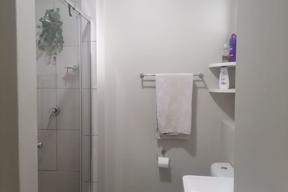 A functional bathroom featuring a glass-enclosed shower, a modern wash basin, a toilet, and built-in corner shelving for storage.