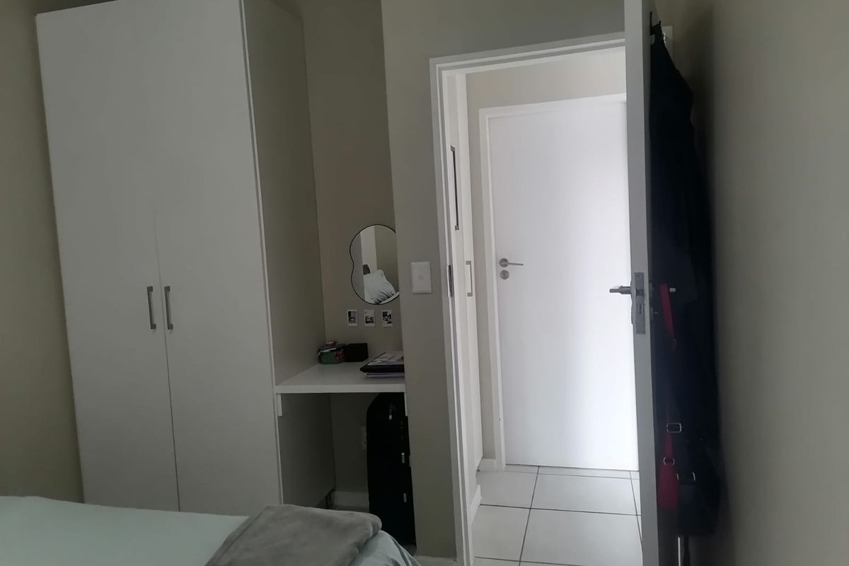 A bedroom featuring a built-in wardrobe and integrated vanity desk, with tiled flooring leading to an adjacent room.