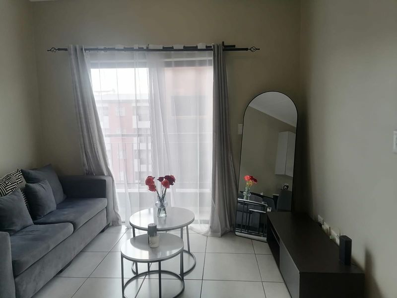 A well-lit living room featuring neutral tiled flooring and a large sliding glass door that provides access to the balcony.