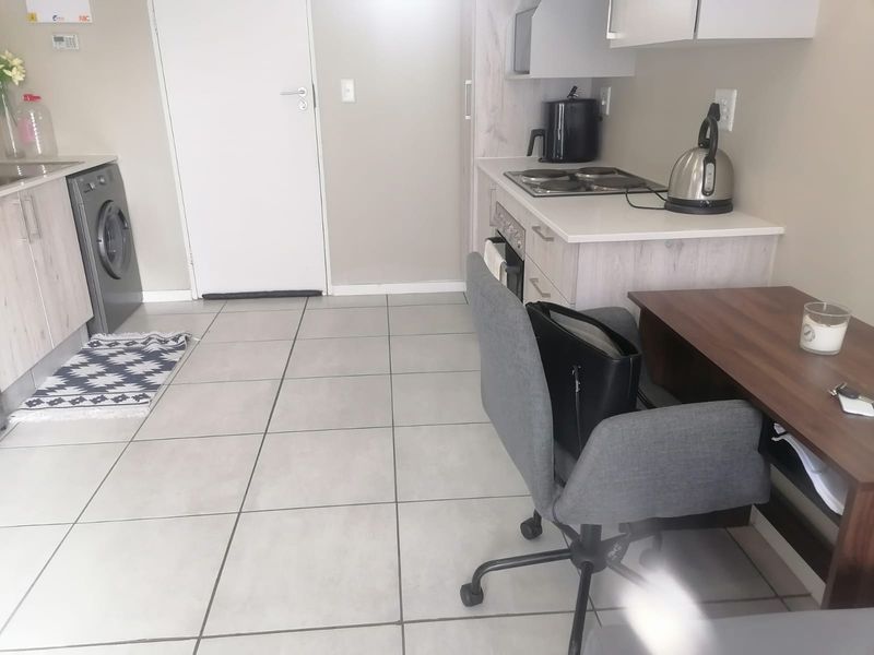 Open-plan kitchen and laundry area featuring tiled flooring, built-in cabinetry, electric hob, and integrated oven in a functional apartment layout.