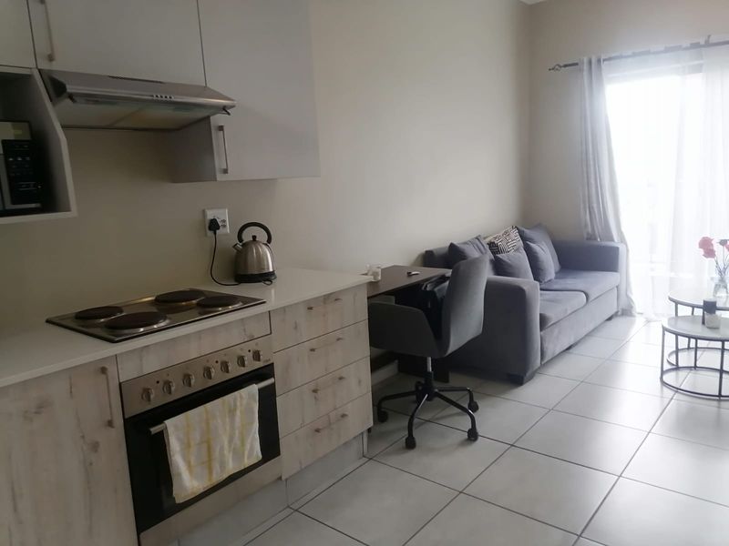 An open-plan living area featuring a modern kitchen with built-in cabinetry, electric hob, oven, and tiled flooring, leading to a bright living space.