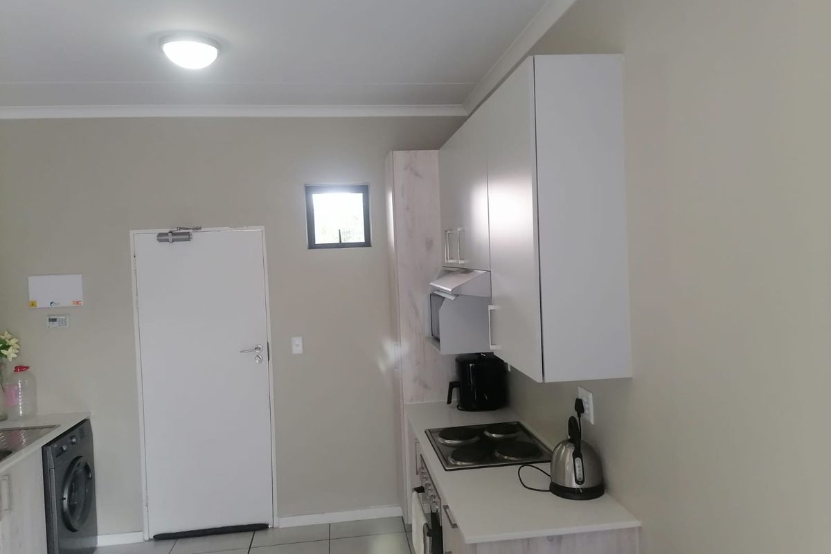Compact kitchen featuring modern built-in cabinetry, electric hob, oven, extractor fan, and tiled flooring, providing a functional and efficient cooking space.