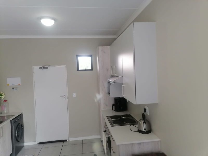 Compact kitchen featuring modern built-in cabinetry, electric hob, oven, extractor fan, and tiled flooring, providing a functional and efficient cooking space.