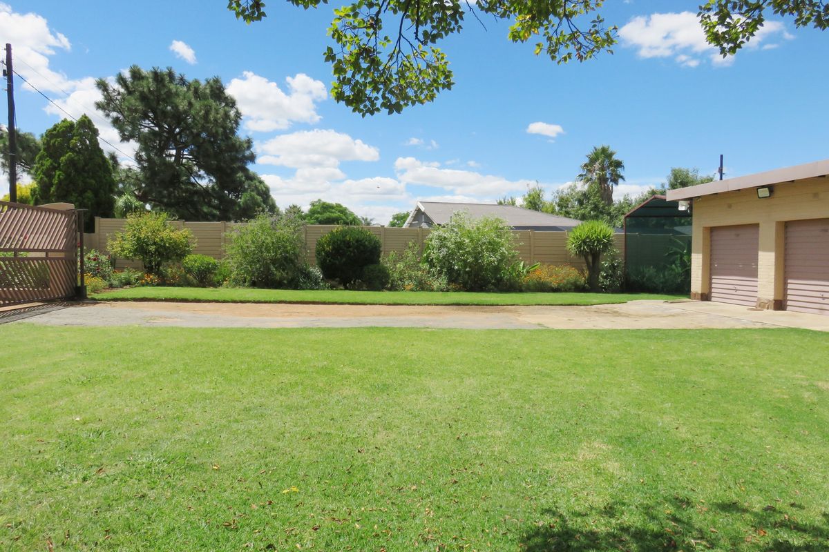 A spacious backyard featuring a well-maintained lawn, established garden beds, perimeter fencing, and a double garage with paved driveway access.