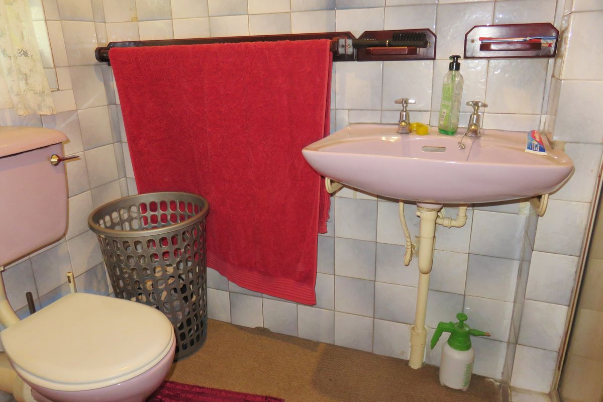 A dated bathroom featuring a vintage pink pedestal basin and matching toilet suite with wall-mounted towel rails and tiled finishes.
