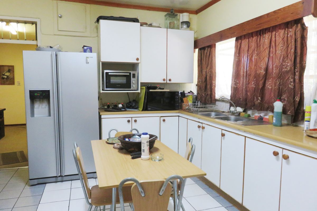 A dated kitchen featuring white cabinetry, laminate countertops, a double sink, and tiled flooring, offering a functional layout with potential for modernization.