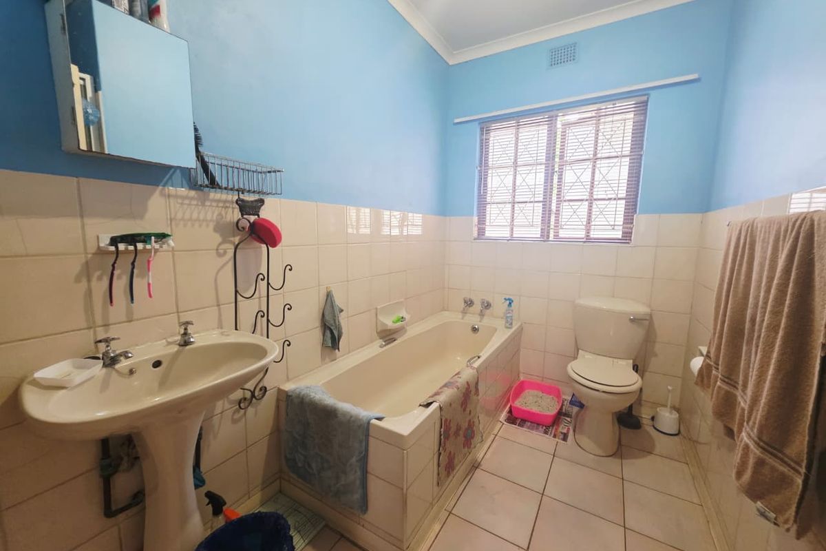 A dated bathroom featuring a pedestal basin, built-in bathtub, and toilet, with tiled walls and flooring. The space would benefit from modern updates.
