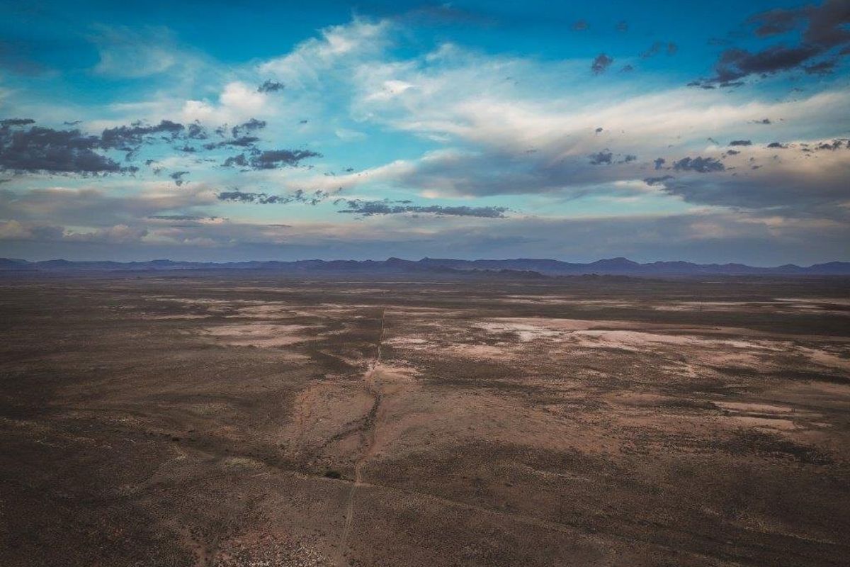 An expansive aerial view of the vast, arid farm landscape under a dramatic cloudy sky, showcasing the property's extensive open terrain.