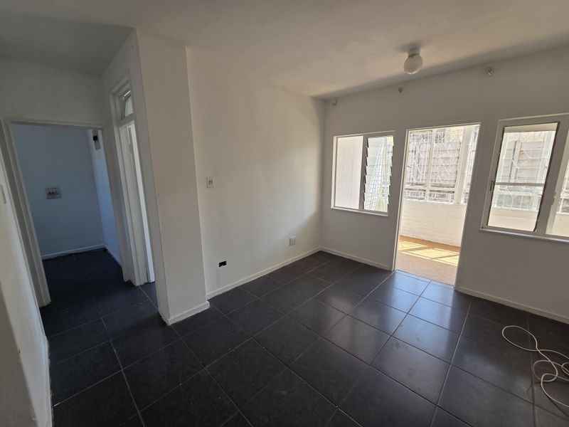An empty living room featuring dark tiled flooring, neutral walls, and direct access to an outdoor balcony area through a sliding door.