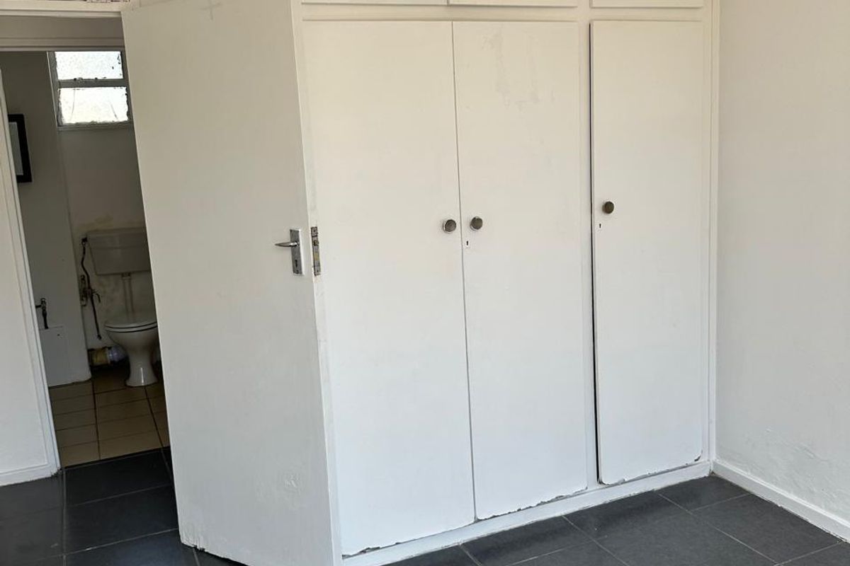 An empty bedroom featuring built-in white cupboards and dark tiled flooring, with an adjacent view into a bathroom area.