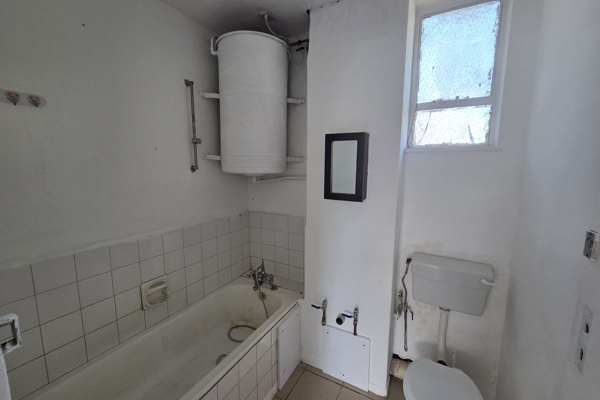 A dated bathroom featuring a bathtub, toilet, and wall-mounted water heater, requiring renovation and cosmetic updates to improve its overall condition and functionality.