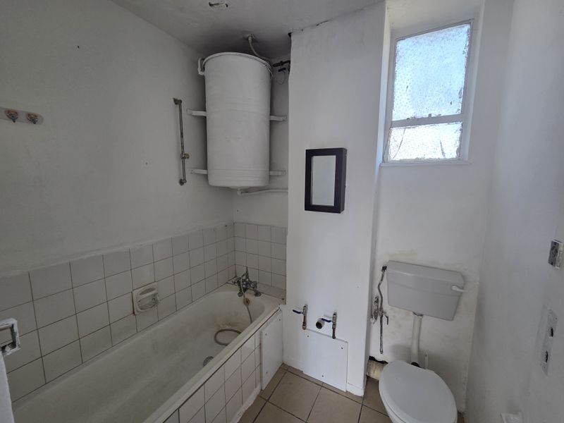 A dated bathroom featuring a bathtub, toilet, and wall-mounted water heater, requiring renovation and cosmetic updates to improve its overall condition and functionality.