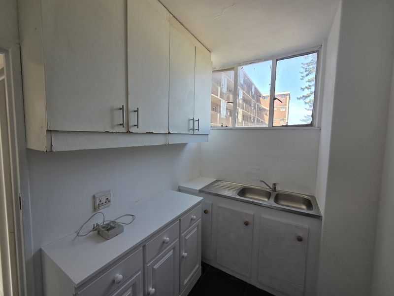 A functional scullery or laundry area featuring built-in white cabinetry, a stainless steel double sink, and a window providing natural light.