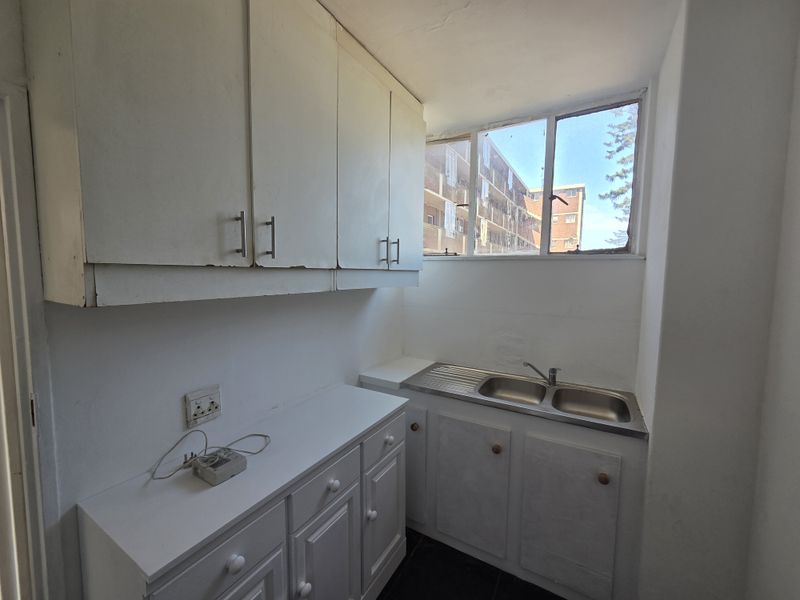 A compact scullery area featuring built-in white cabinetry, a stainless steel double sink, and a window providing natural light.
