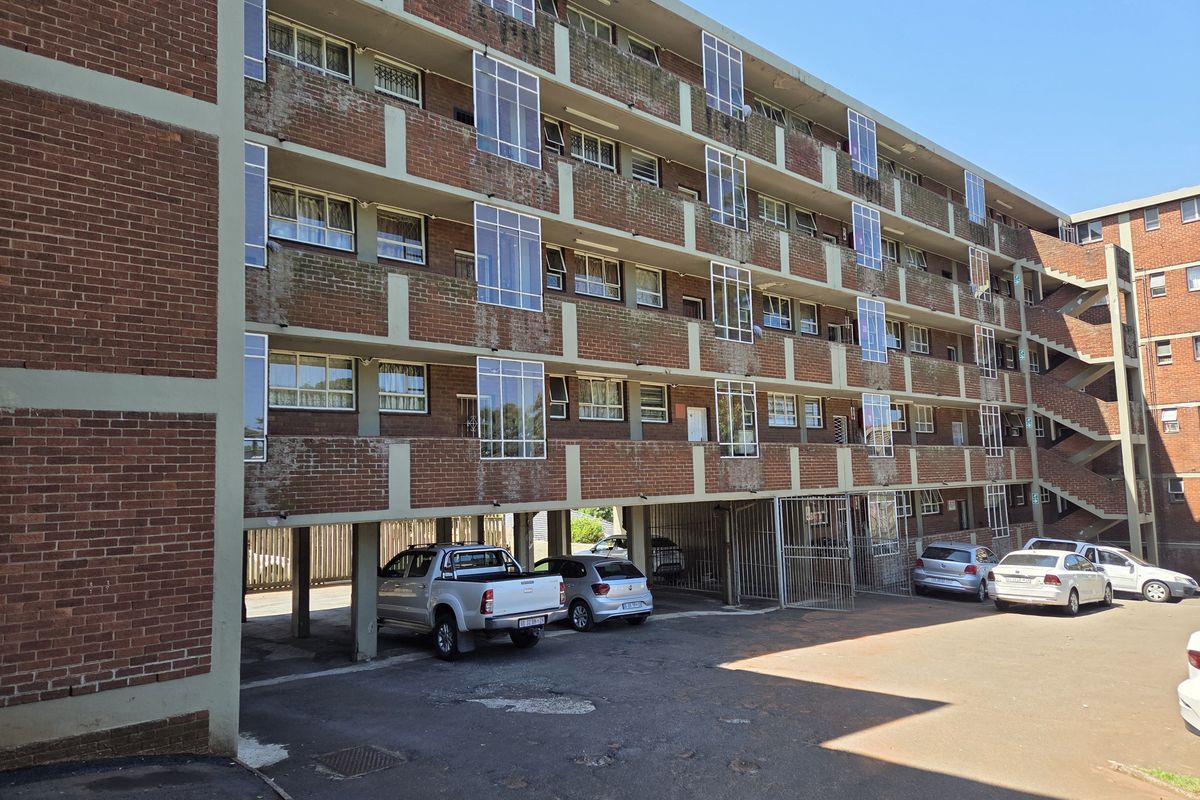 Exterior view of a multi-story brick apartment building featuring covered ground-level parking and open balcony access.