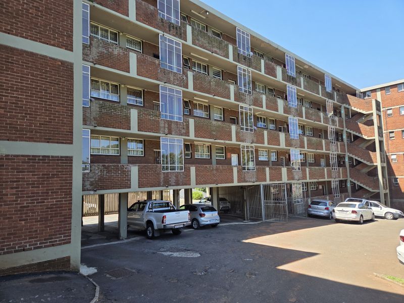 Exterior view of a multi-story brick apartment building featuring covered ground-level parking and open balcony access.