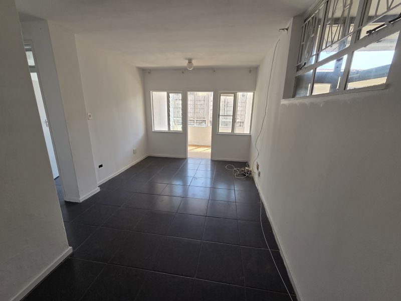 An empty, open-plan living area featuring dark tiled flooring, white walls, and direct access to an outdoor balcony space.