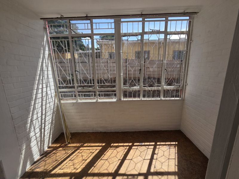 An enclosed sunroom or patio area featuring painted brick walls, large windows with security bars, and worn flooring.
