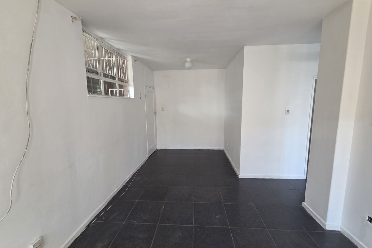 An empty, open-plan living area featuring dark tiled flooring, white walls, and a window with security bars.
