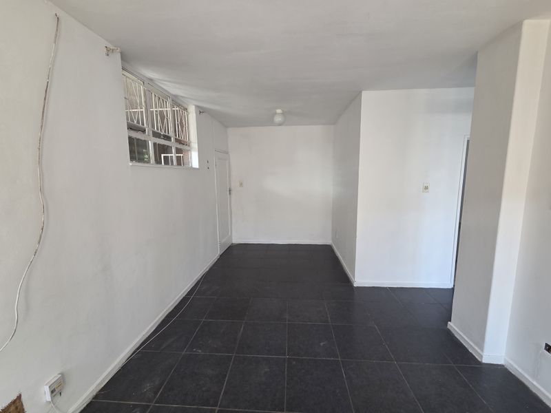 An empty, open-plan living area featuring dark tiled flooring, white walls, and a window with security bars.