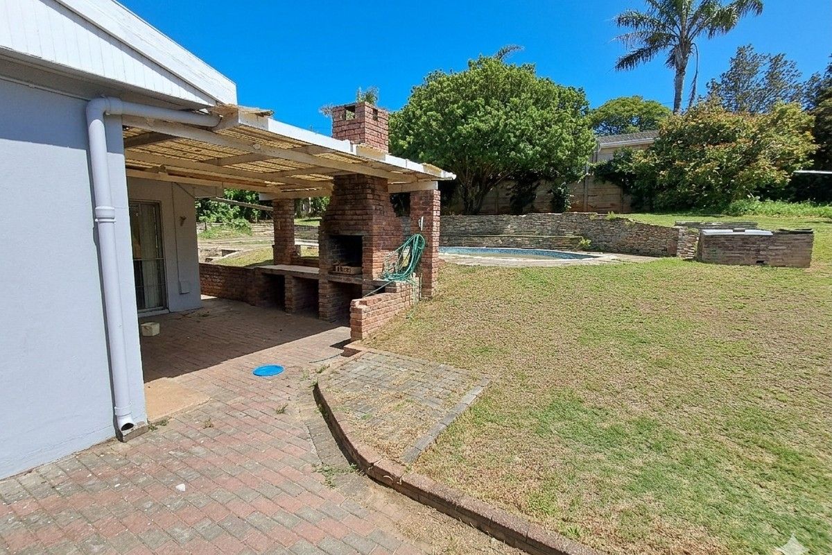 Rear garden featuring a covered patio with a built-in brick braai, swimming pool, and tiered retaining walls.