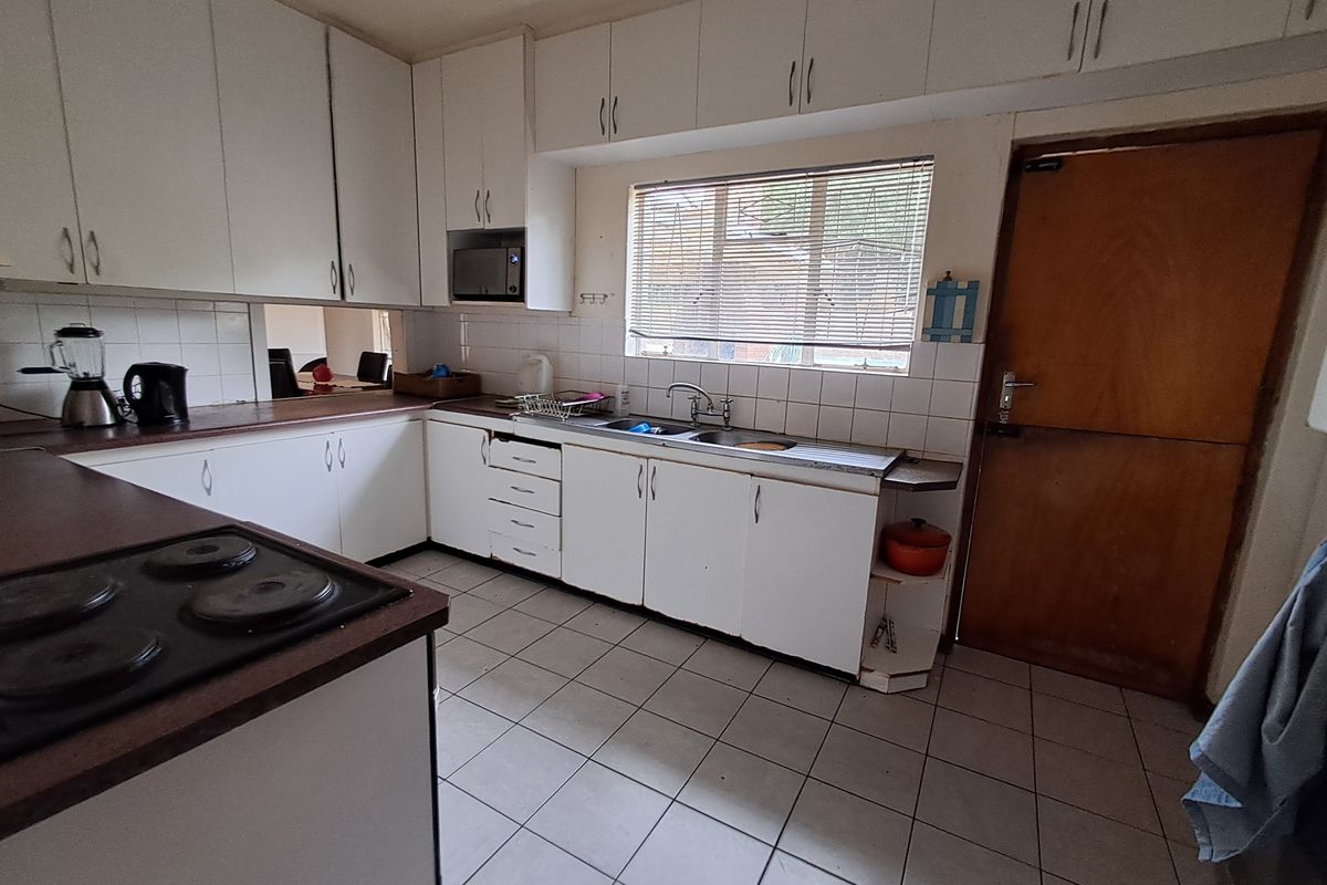 A functional kitchen featuring white cabinetry, laminate countertops, an electric hob, and tiled flooring, offering a dated aesthetic ready for modernization.