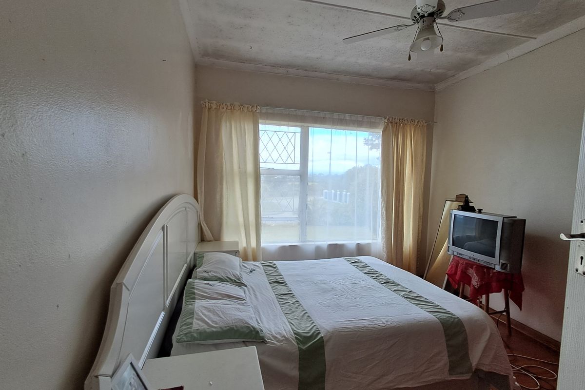 A bedroom featuring a ceiling fan and a window with security bars. The room requires cosmetic updates, particularly to the ceiling finishes.