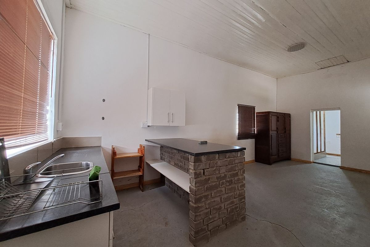 A functional kitchen area featuring a brick-base breakfast bar, stainless steel sink, and basic cabinetry, set within a room with exposed ceiling finishes.
