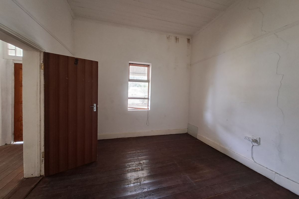An empty bedroom featuring original timber flooring, a single window, and visible signs of wear including wall cracks and ceiling water marks.