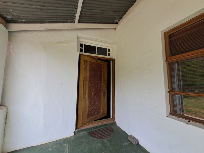 A covered entrance porch featuring a carved wooden front door, transom window, and painted concrete flooring.