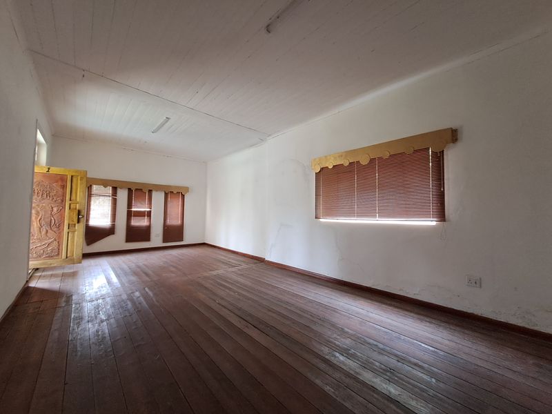 An empty, spacious room featuring original timber flooring, white painted timber ceiling, and multiple windows with fitted blinds.