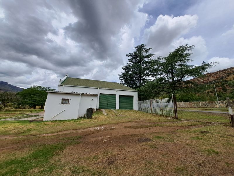 A detached garage building featuring a pitched roof, dual green roller doors, and white exterior walls, situated on a grassed lot.